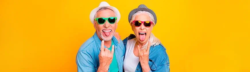 Un homme et une femme seniors, portant chapeaux et de lunettes de solei, profitent de leur retraite en tirant la langue et en souriant.