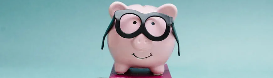 tirelire cochon rose portant des lunettes, posée sur un livre.