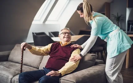 Un homme âgé qui est assis dans un canapé souriant à son aide à domicile. 