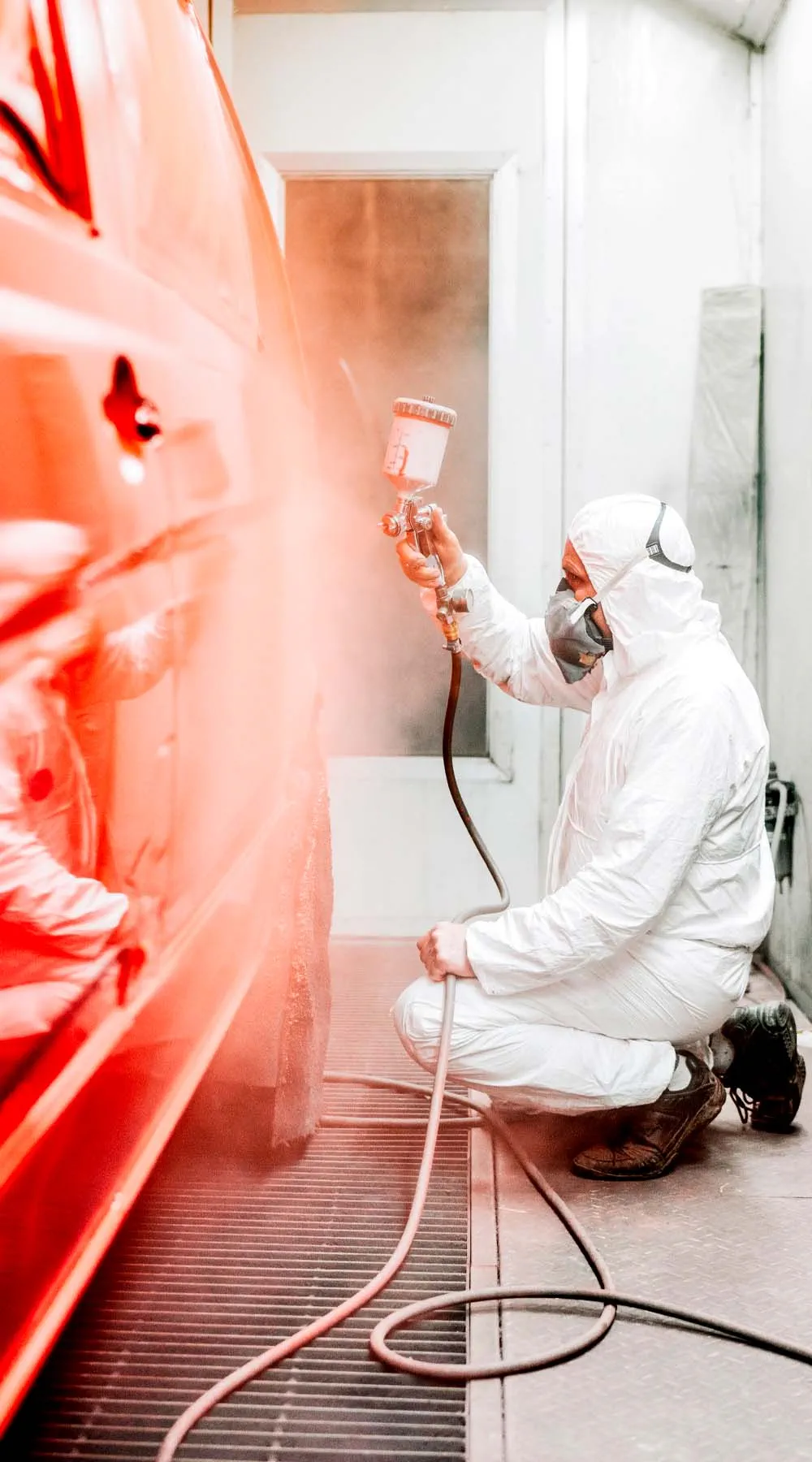 Trabajador pintando un vehículo con pistola en una cabina de pintura industrial