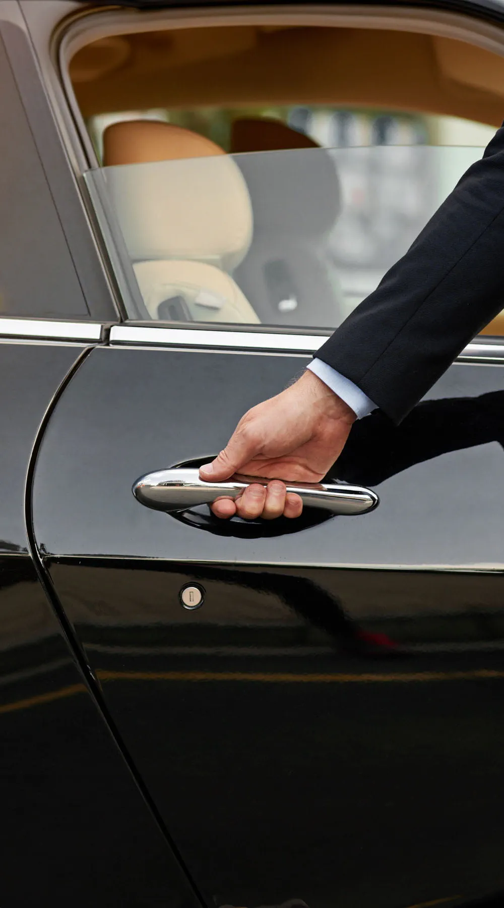 Mano de un hombre vestido de traje sujetando la manivela de una puerta de un coche