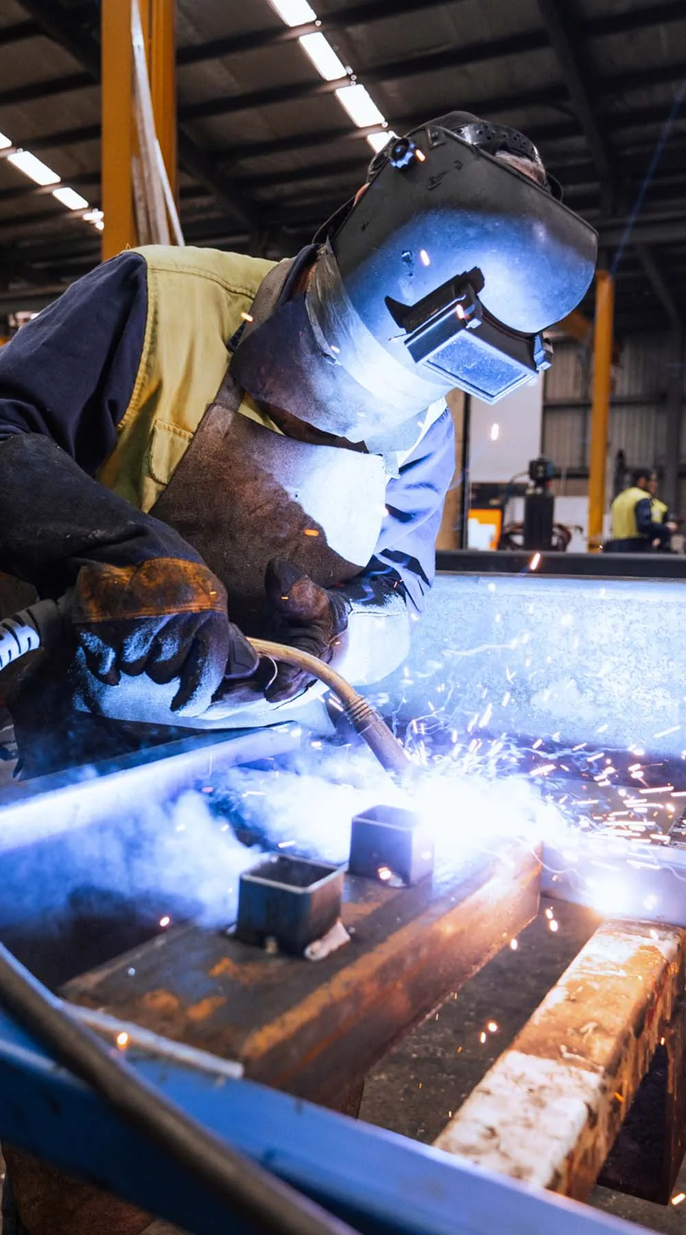 Trabajador con equipo de protección soldando metal en un entorno de fábrica industrial