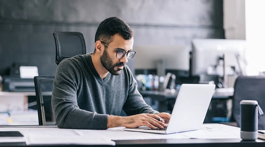 Hombre con gafas revisa seria información en un ordenador portátil