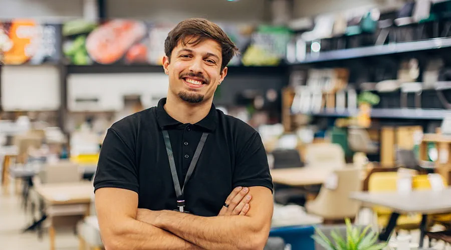 Vendedor en una tienda de muebles mira directamente a la cámara mientras está de pie en la tienda