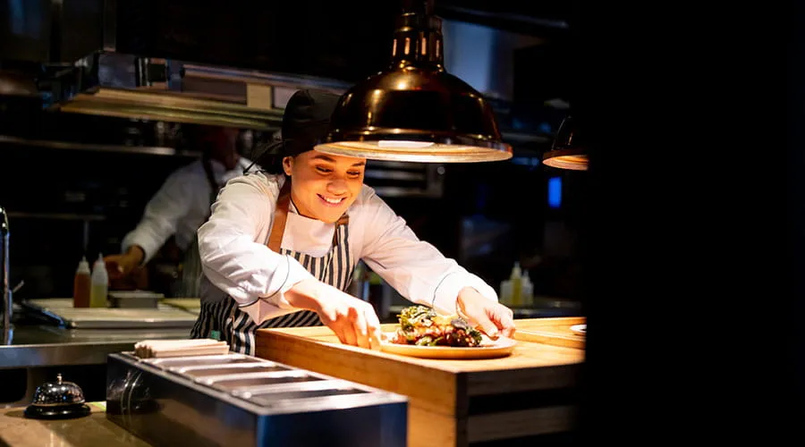 Chef colocando un plato bajo una lámpara caliente en una cocina comercial
