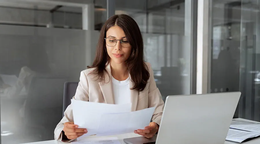 Mujer joven en entorno de oficina leyendo documentos financieros