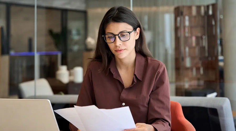 Mujer joven en entorno de oficina leyendo documentos financieros