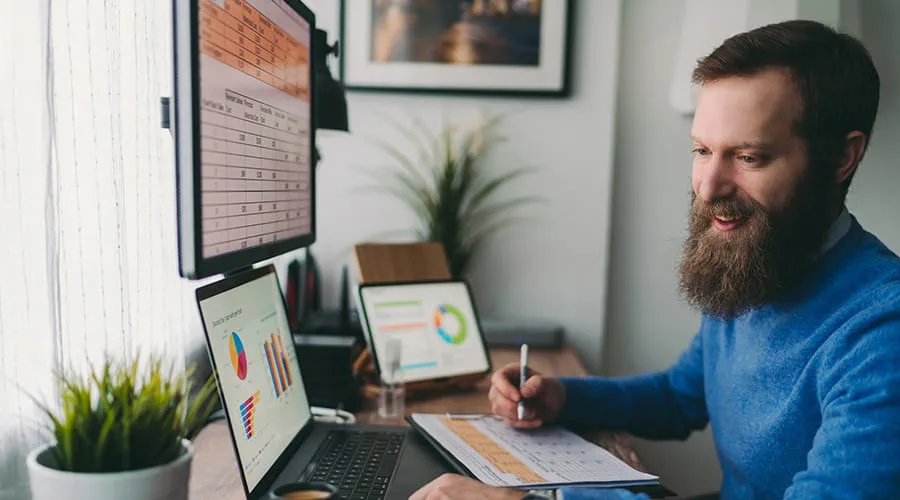 Hombre trabajando con varias pantallas con datos y gráficos