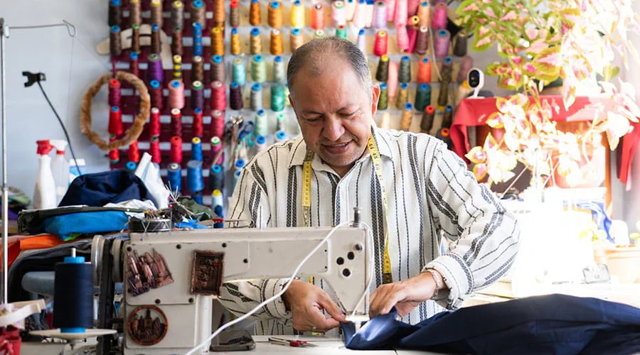 Costurero latino cosiendo con su máquina de coser en su taller de costura