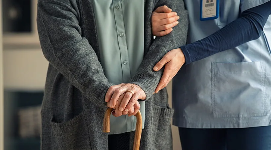 Enfermera sujetando por el brazo a una persona de avanzada edad
