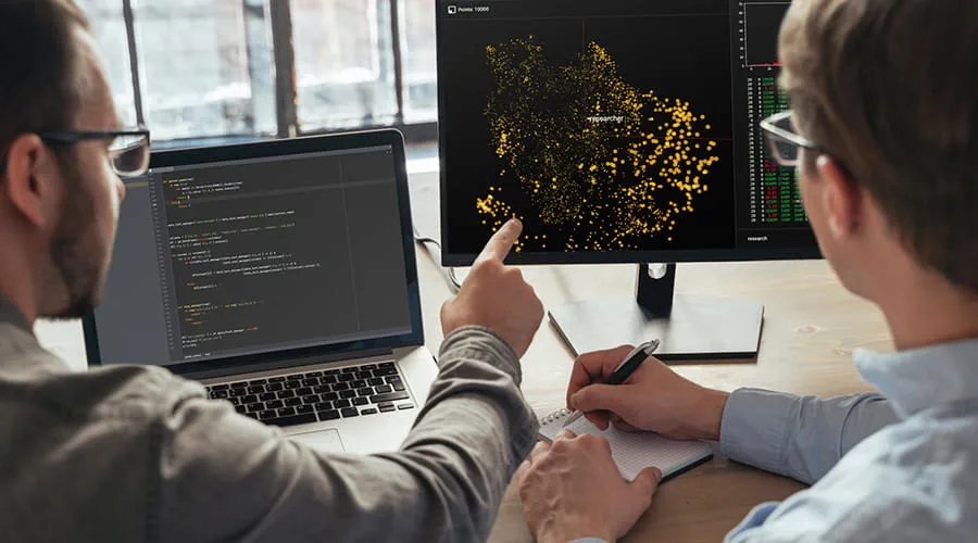 Dos hombres señalando un monitor con datos