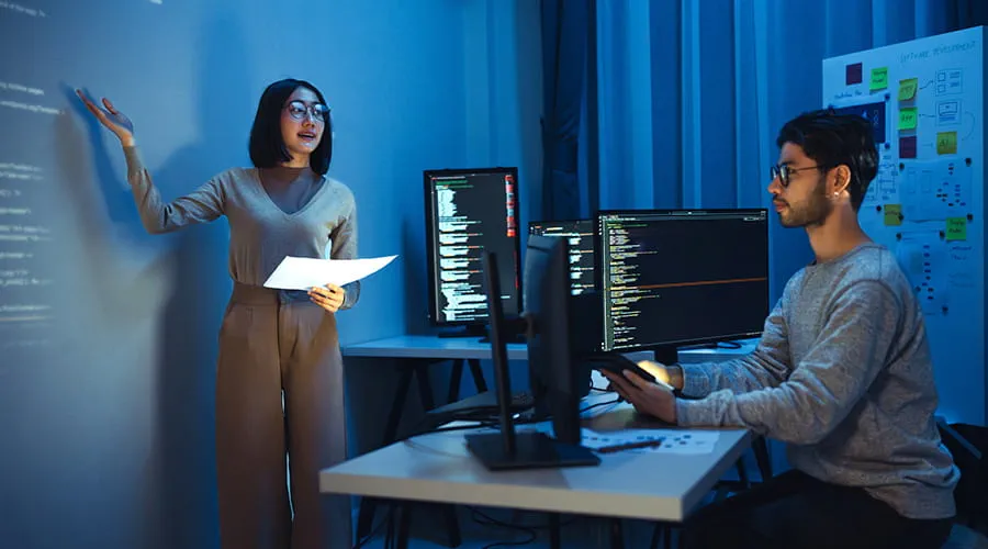 Programadora asiática de pie frente a una pantalla con una presentación proyectada en código