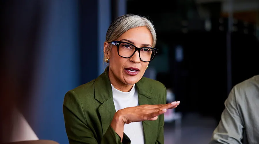 Mujer de negocios con cabello gris y gafas, gesticulando y explicando