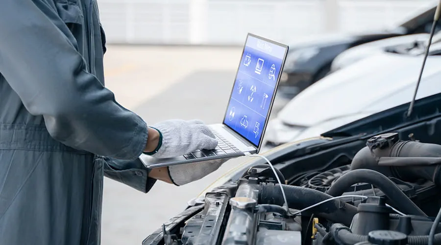 Mecánico utilizando una computadora portátil para comprobar la recopilación de información durante el trabajo de un motor de coche