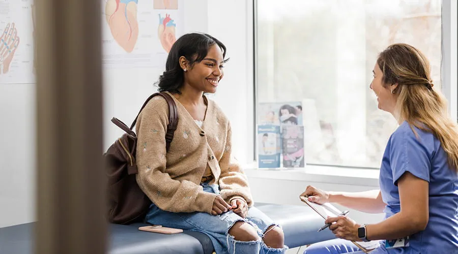 Paciente adulta joven sonríe mientras escucha a la enfermera dar una actualización sobre su examen médico