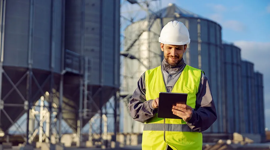 Hombre con casco revisando una tablet en entorno agrícola