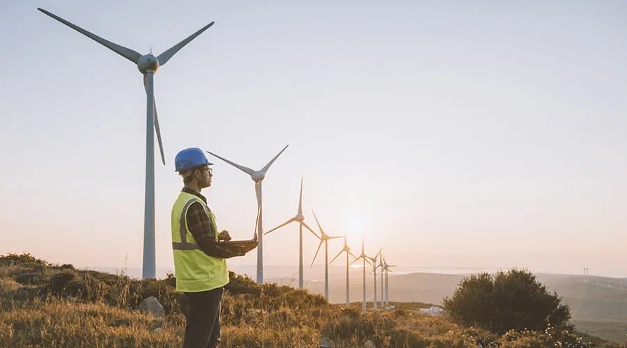 Hombre con casco entre molinos de viento de energía eólica