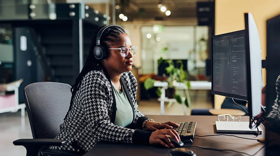 Programadora informática con auriculares codificando en una oficina moderna