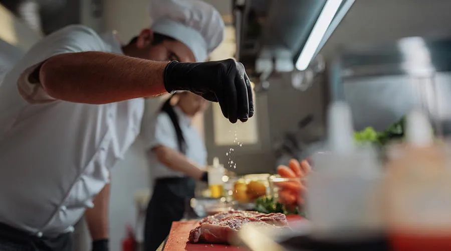 Chef espolvoreando sal sobre la carne cruda en una cocina profesional