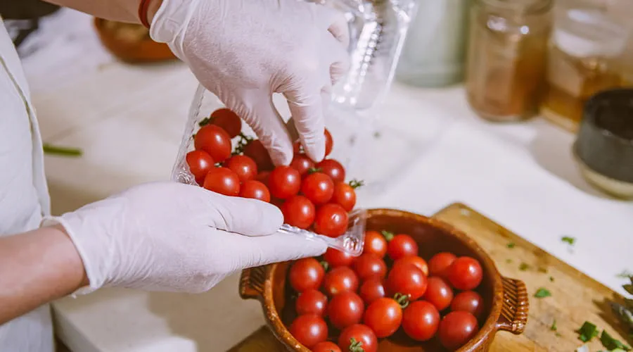 Manos con guantes manipulando unos tomates para servir después