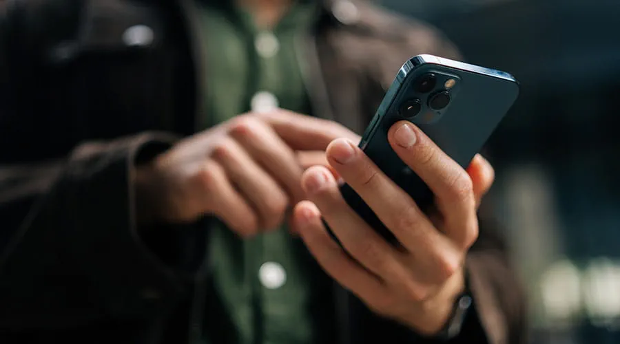 Manos en primer plano de un hombre que sostiene un teléfono inteligente de pie en la calle