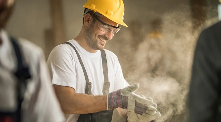 Feliz trabajador limpia sus guantes de serrín en el sitio de construcción