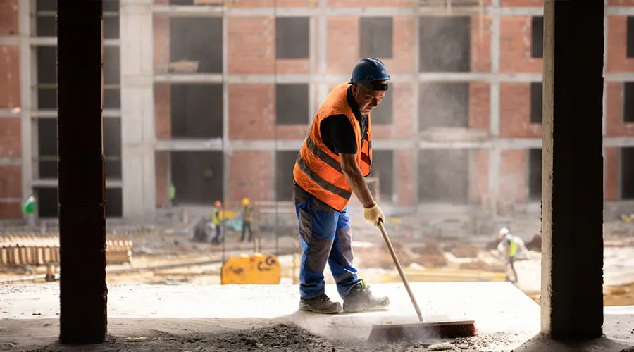 Trabajador usando escoba para limpiar el polvo en el sitio de construcción