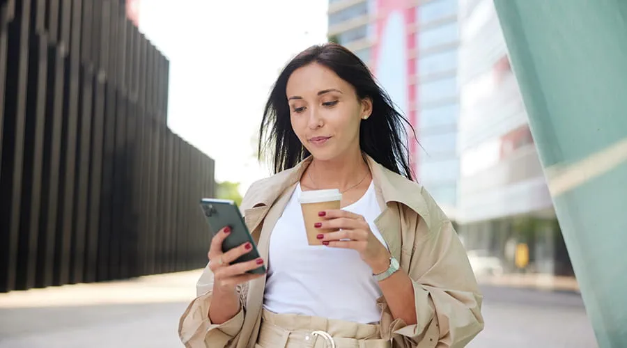 Mujer joven antando por la calle revisando su teléfono inteligente