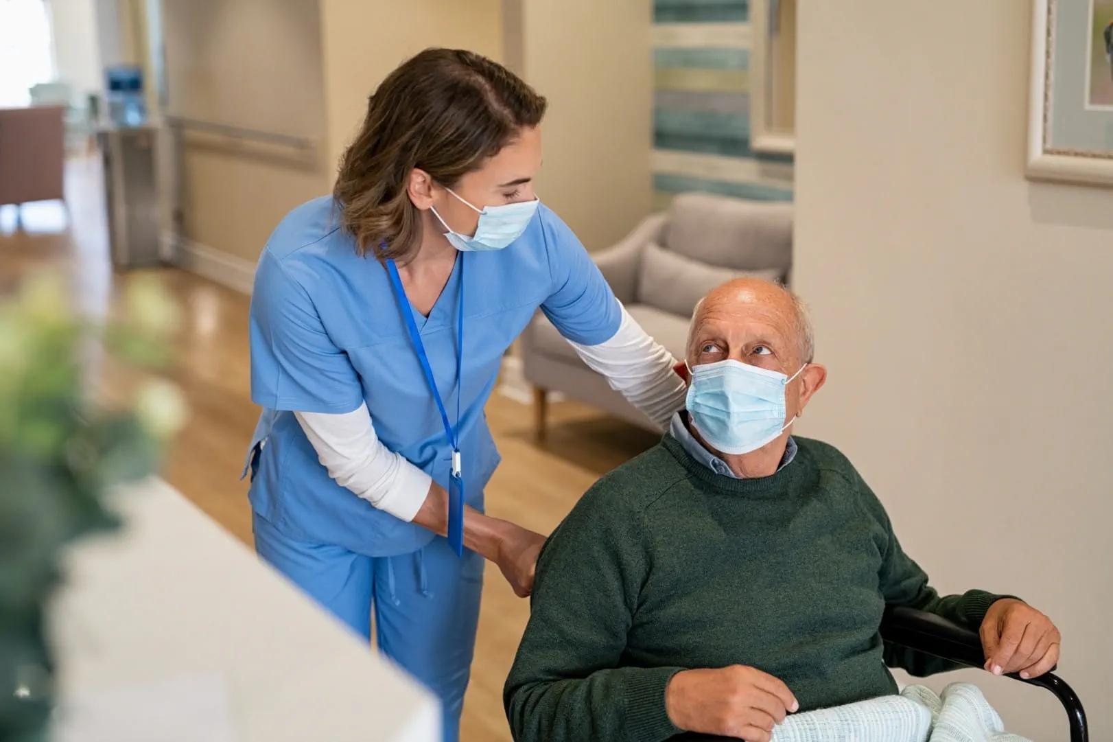 Une infirmière portant un masque aide un patient âgé en fauteuil roulant