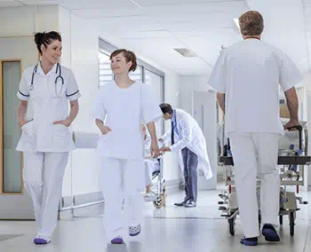 Deux infirmières souriantes marchent dans le couloir d'un hôpital et un infirmier pousse un brancard à côté