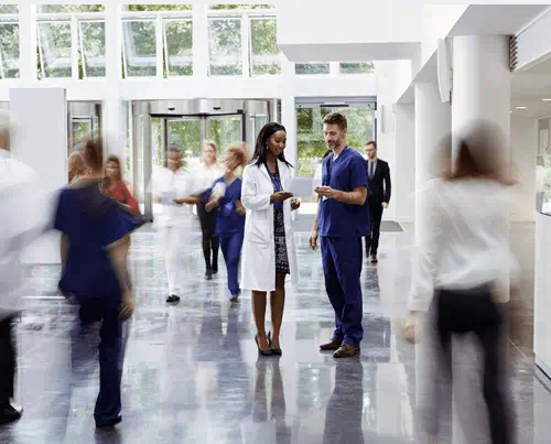 Un hall d'hôpital moderne et animé avec au centre une femme et un homme en blouse discutant et des personnes se déplacent autour