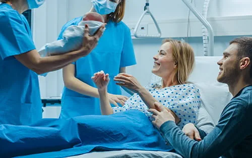Une soignante présente un nouveau-né à une mère souriante et à son partenaire dans une salle d'accouchement d'hôpital
