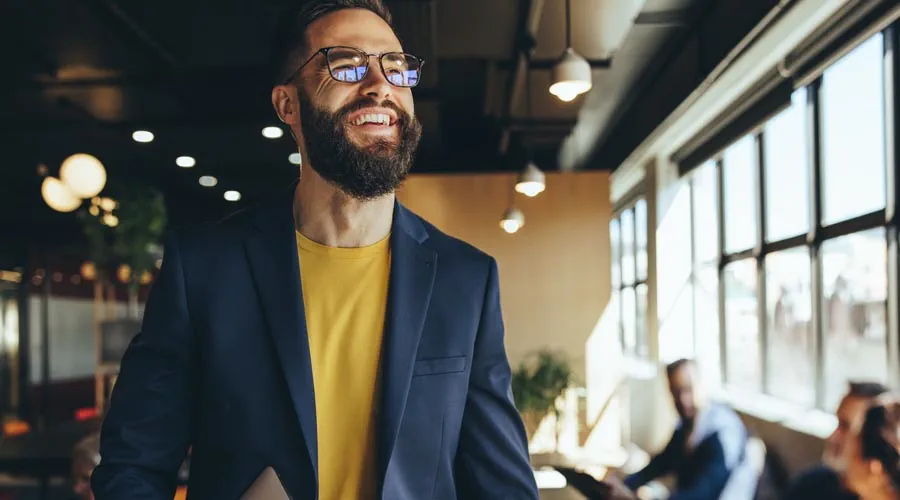 Male professional holding a laptop and smiling in a modern office
