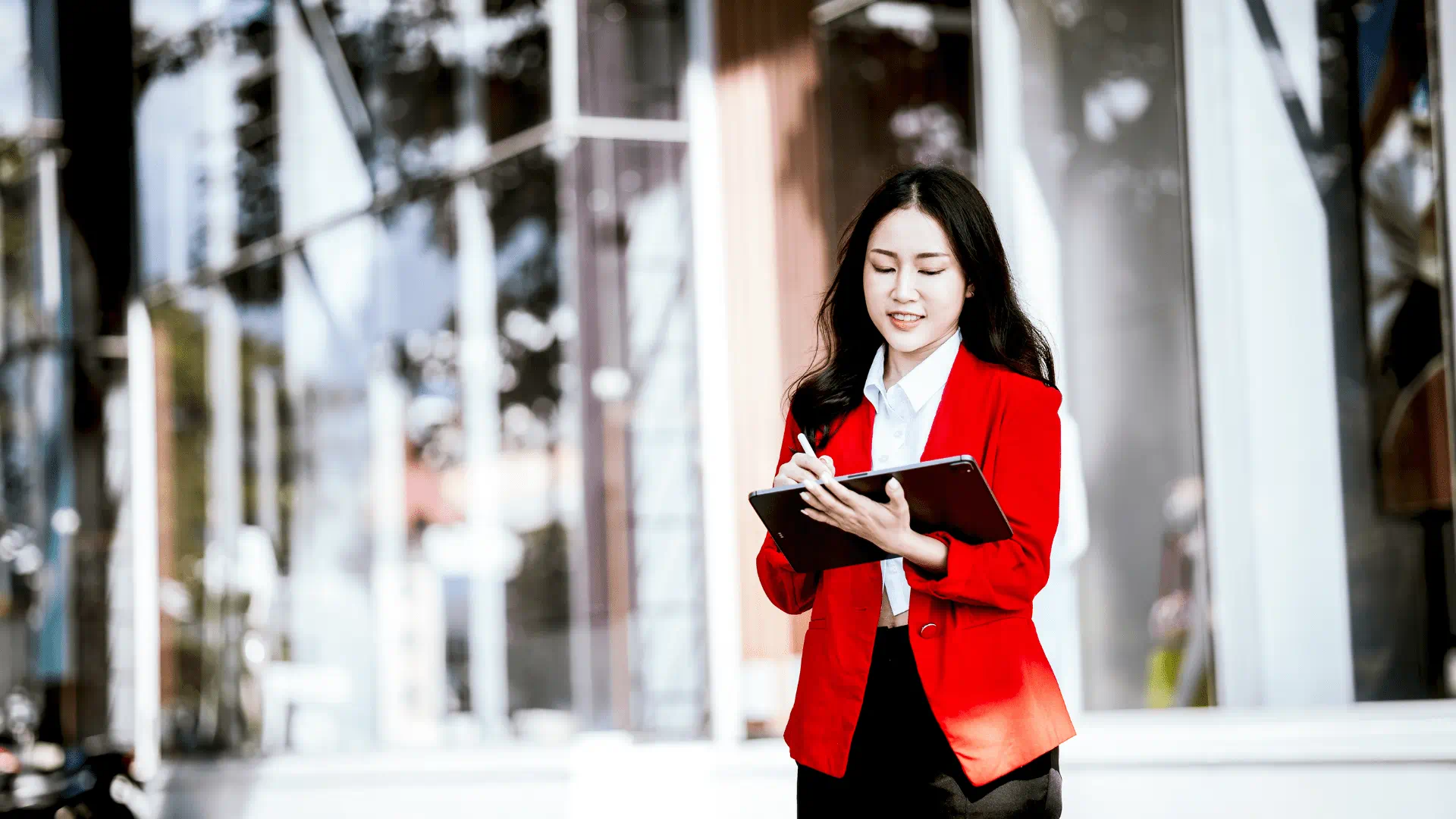 woman with a red blazer standing outside writing in her notebook