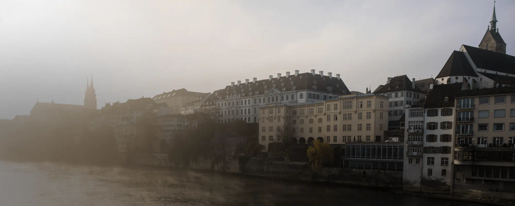 Sponde del fiume avvolte dalla nebbia, con edifici storici e campanili parzialmente nascosti dalla foschia.