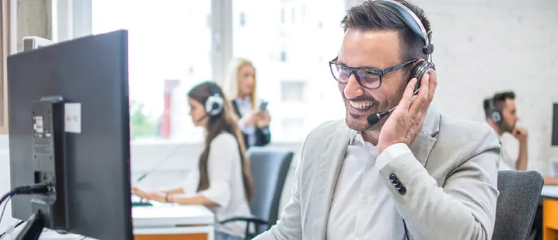 Person smiling while wearing a headset working in a modern call center with colleagues in the background