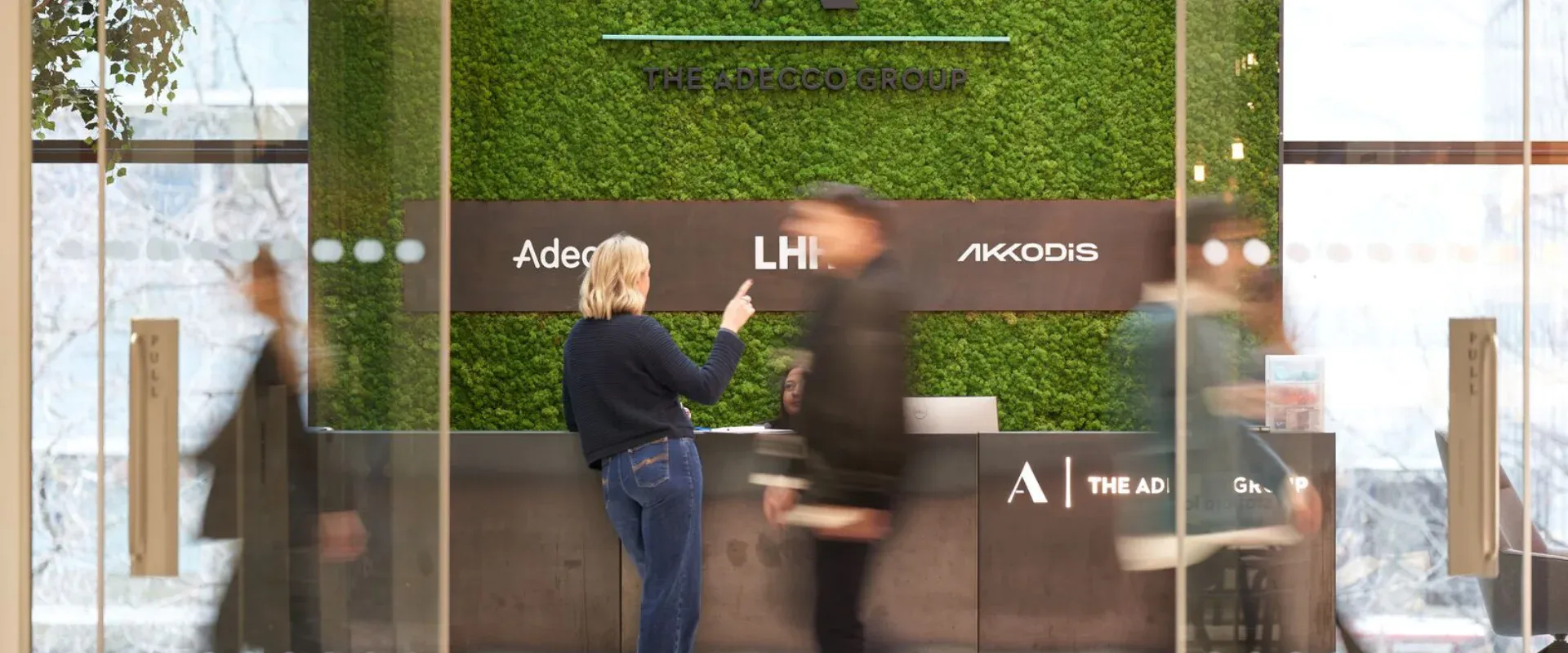 Receptionen på ett av Adeccos kontor i  världen. Människor rör sig förbi i bakgrunden, vilket skapar en dynamisk och livlig atmosfär.