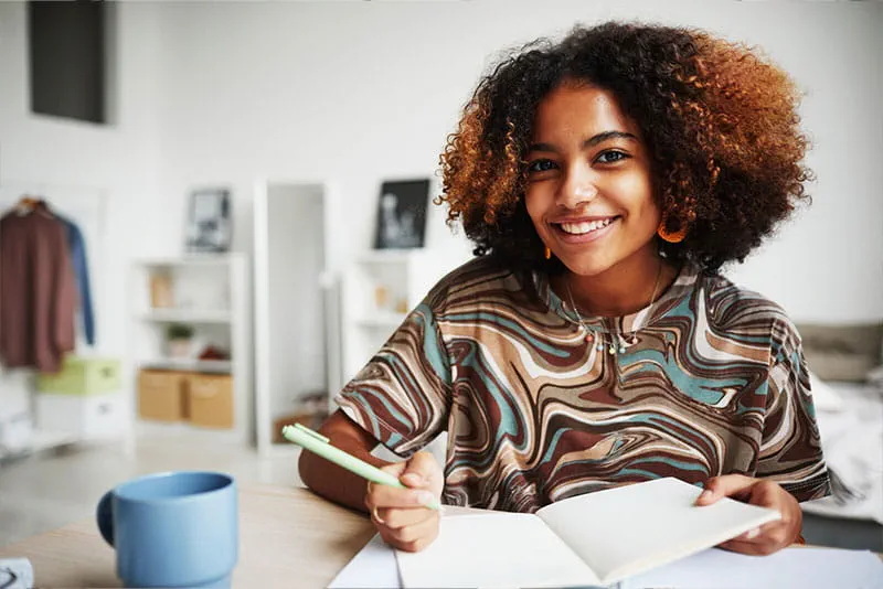 Woman writing notes in a notebook while smiling at a desk