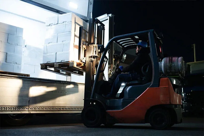 Forklift operator loading pallets onto a delivery truck at a busy warehouse during peak season.