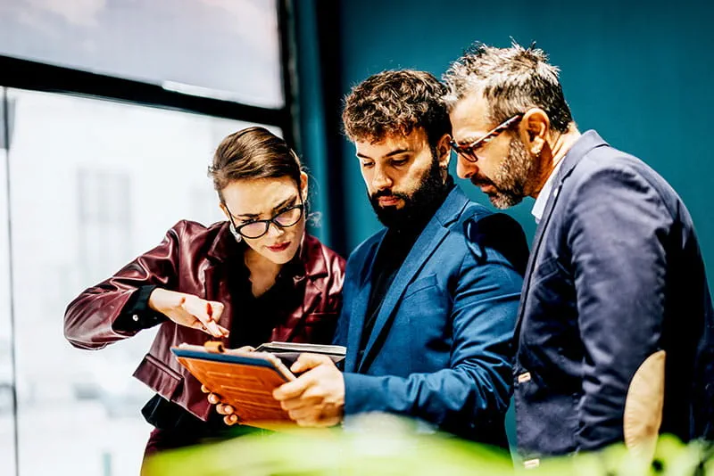 Three professionals reviewing information together on a tablet during a discussion in a modern office.