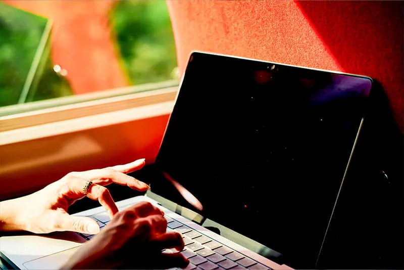 Close-up of a person using a laptop while travelling, with sunlight streaming through a window.
