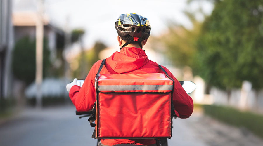 Repartidor montado en una bicicleta de espaldas con una mochila de color rojo