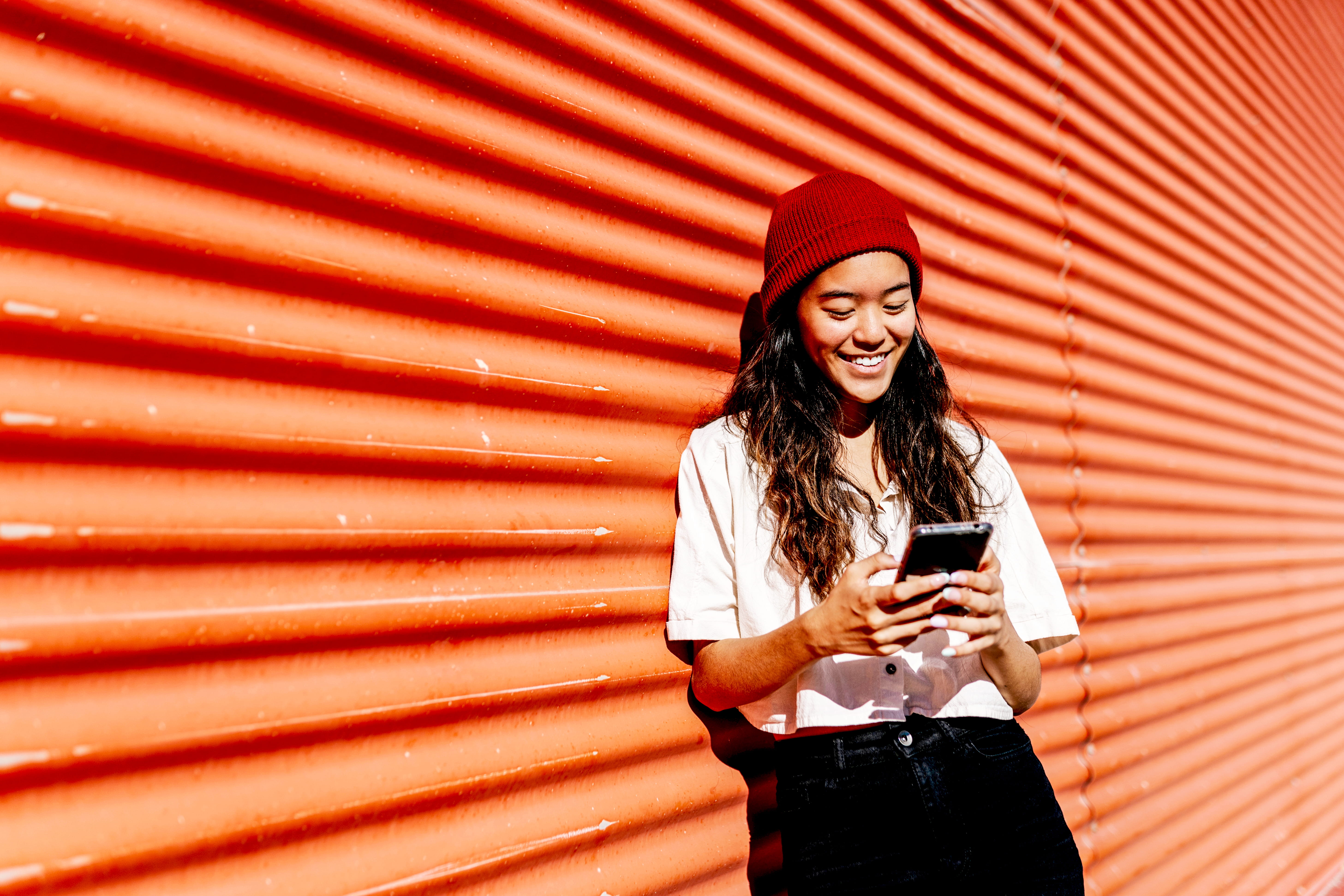Smiling woman using mobile phone at red corrugated wall