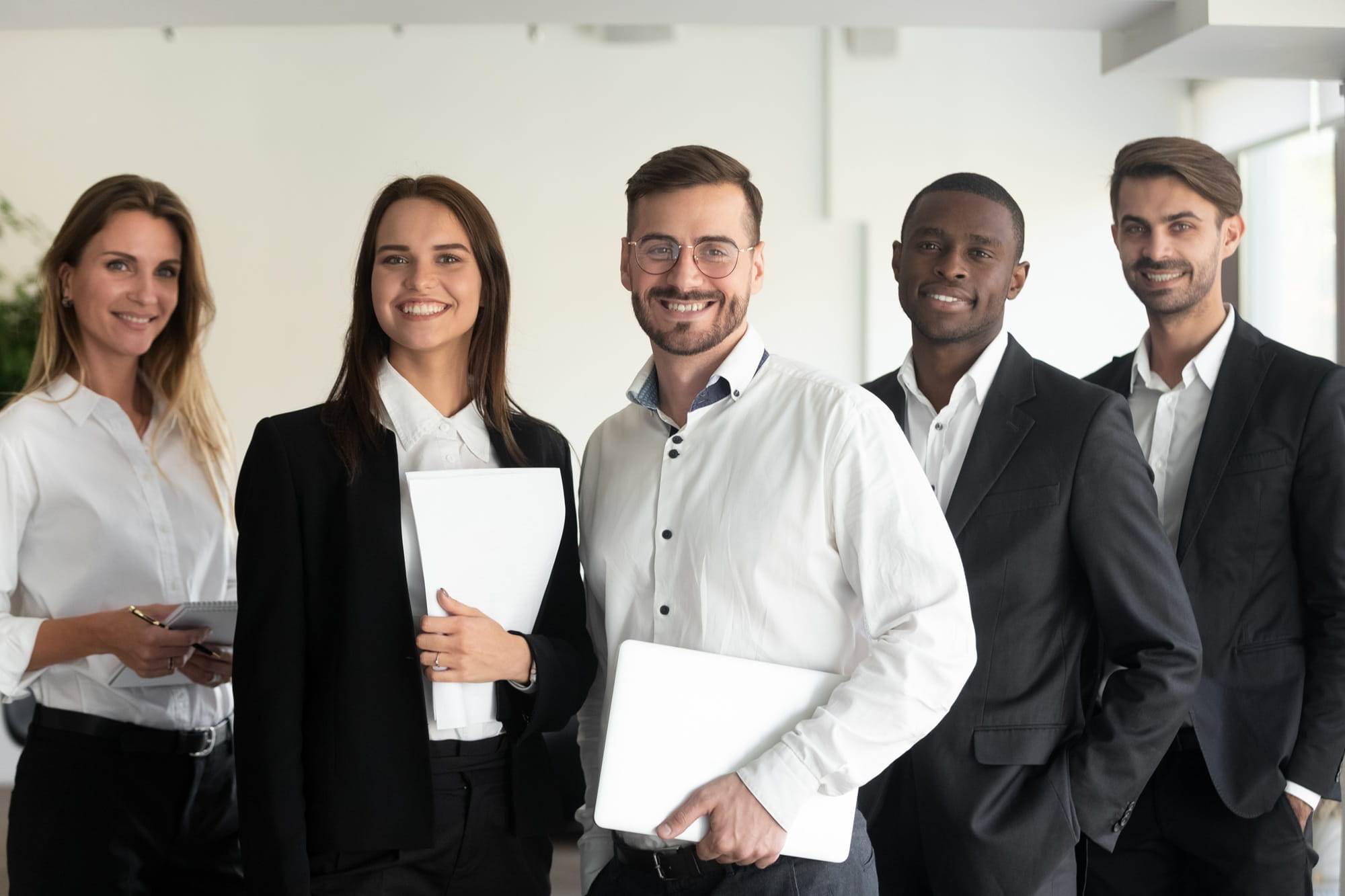 Smiling, confident, and diverse business team standing together in an office, looking at the camera