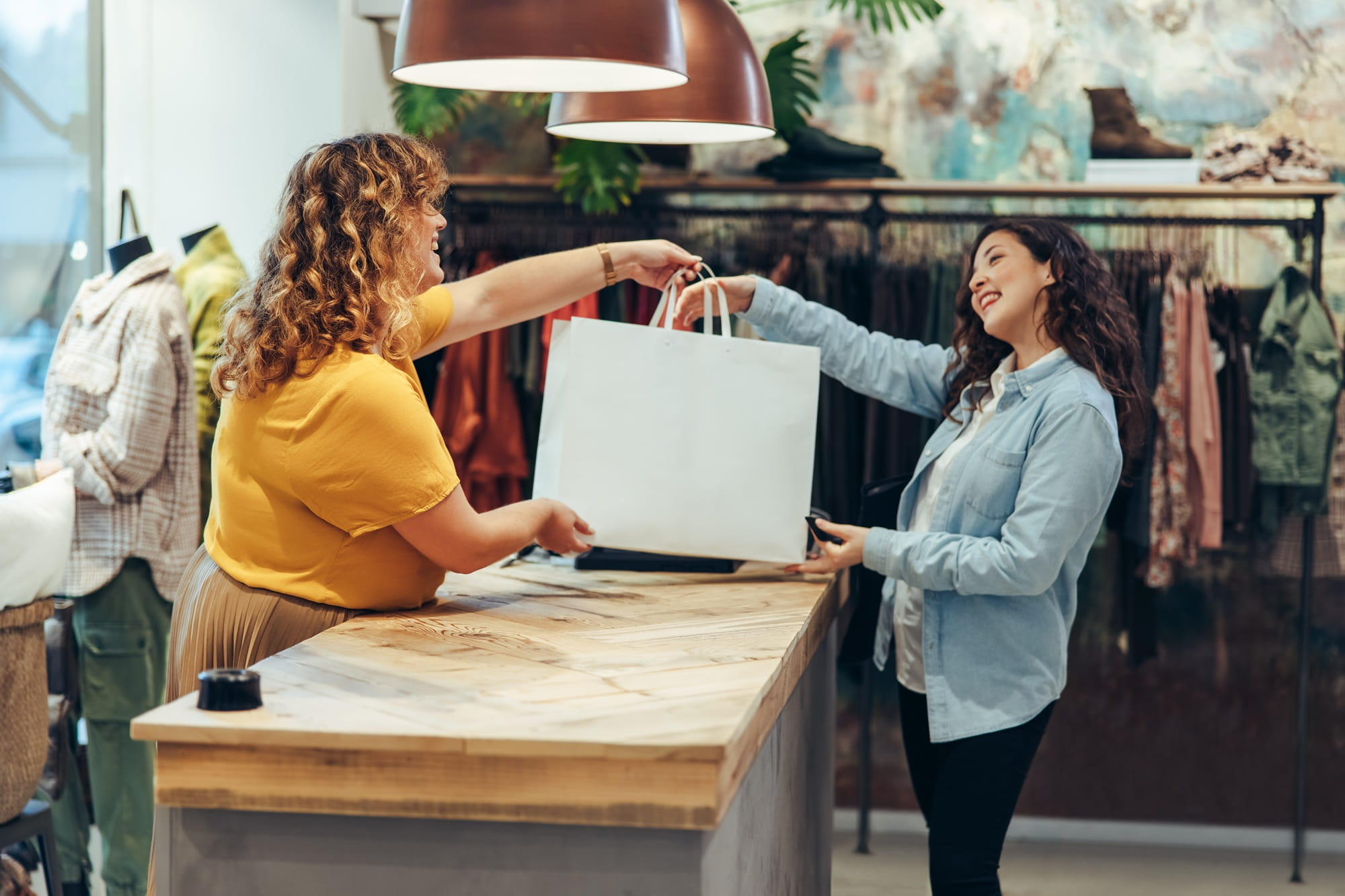 Une cliente souriante et une conseillère de vente se tiennent ensemble dans un magasin avec un sac.