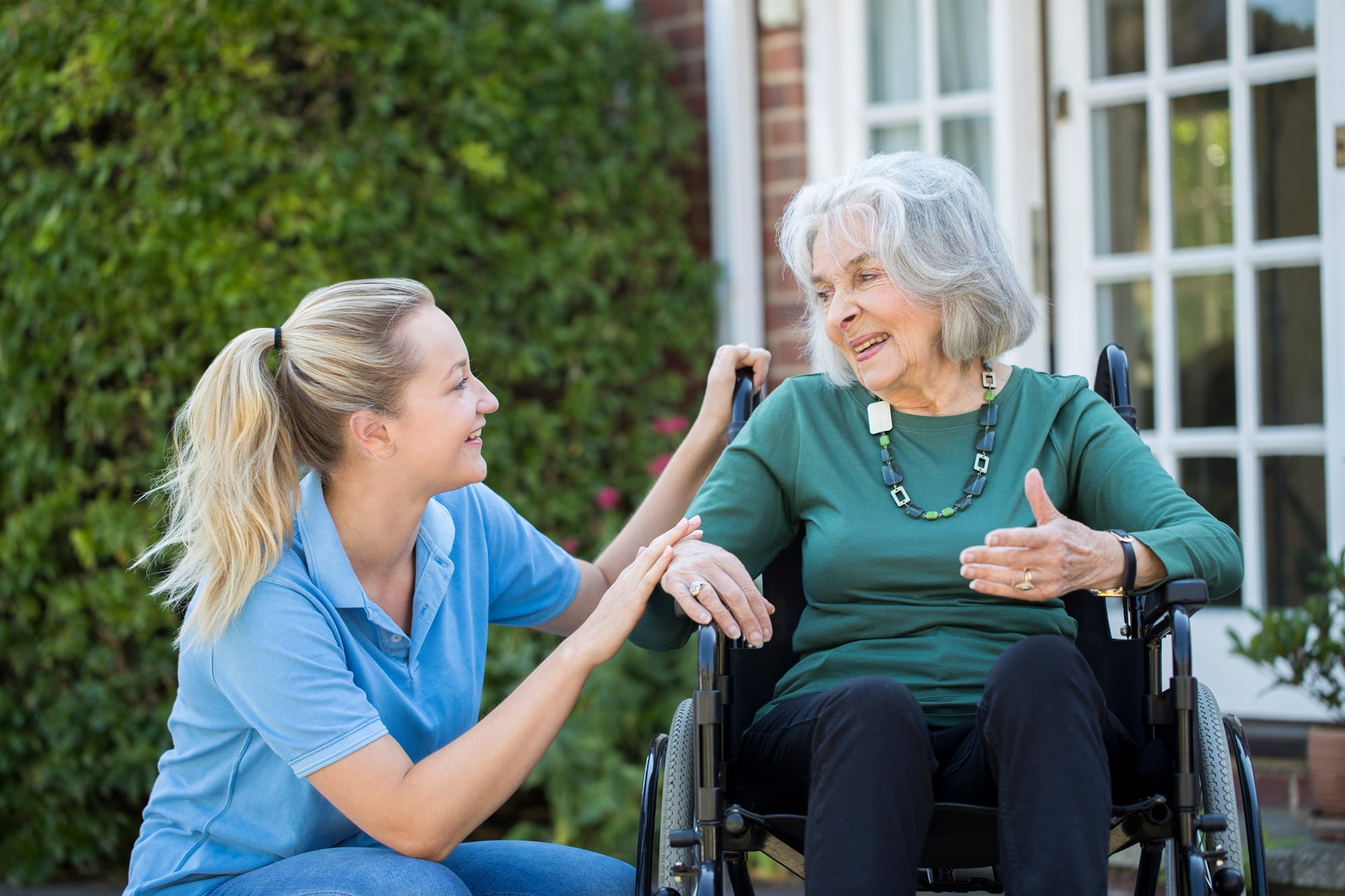  Eine Krankenschwester spricht mit einer älteren Frau im Rollstuhl.