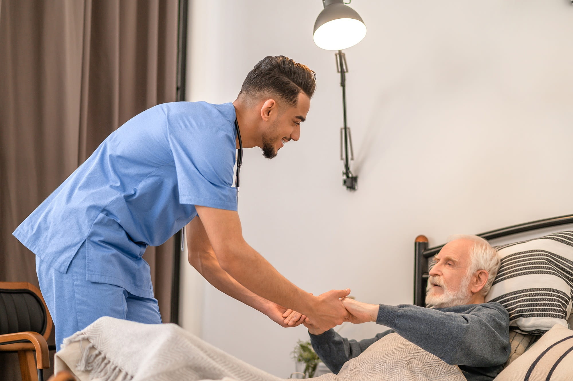 Ein Krankenpfleger hilft einem älteren Mann, aus dem Bett aufzustehen.