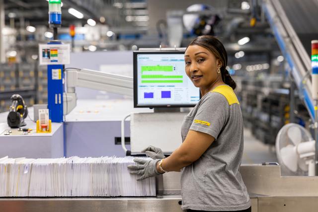 An employee operates a sorting machine and organizes letters, with processing data visible on the monitor.