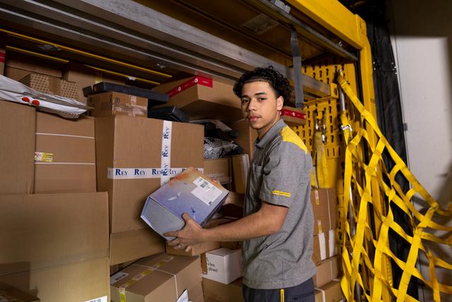 An employee lifts a parcel from a delivery vehicle filled with stacked boxes.