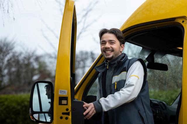 An employee opens the door of a yellow delivery vehicle.